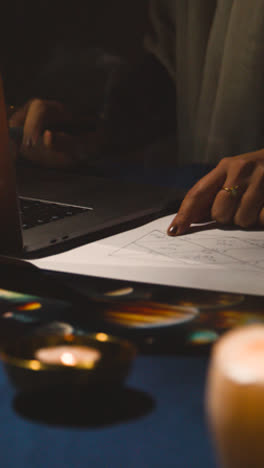 Vertical-Video-Close-Up-Of-Woman-Using-Laptop-To-Draw-Astrology-Lagna-Or-Birth-Chart-On-Candlelit-Table